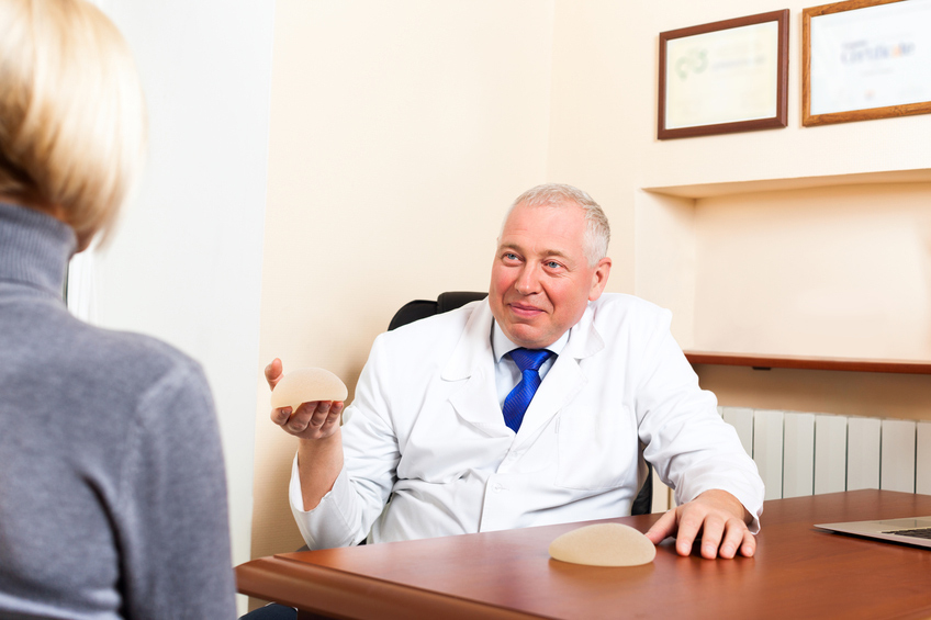 doctor talking to young woman patient, show silicone breast implant at office desk, plastic surgery consultation